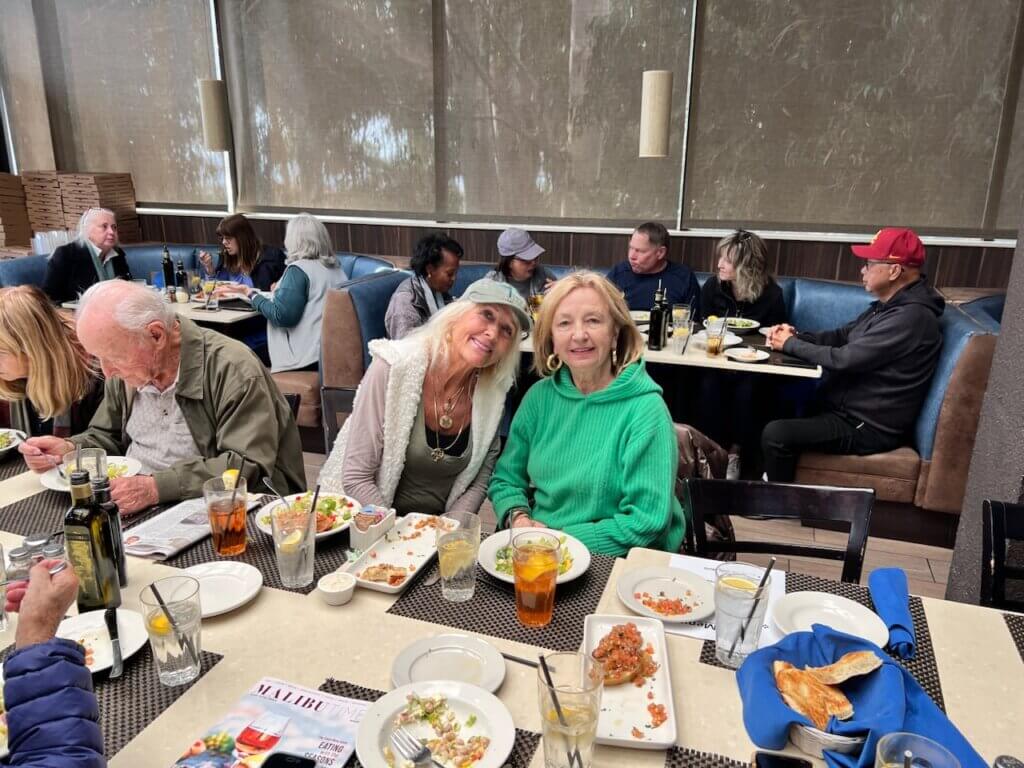 Two Malibu Garden Club members posing for a photo while other members dine at Spruzzos